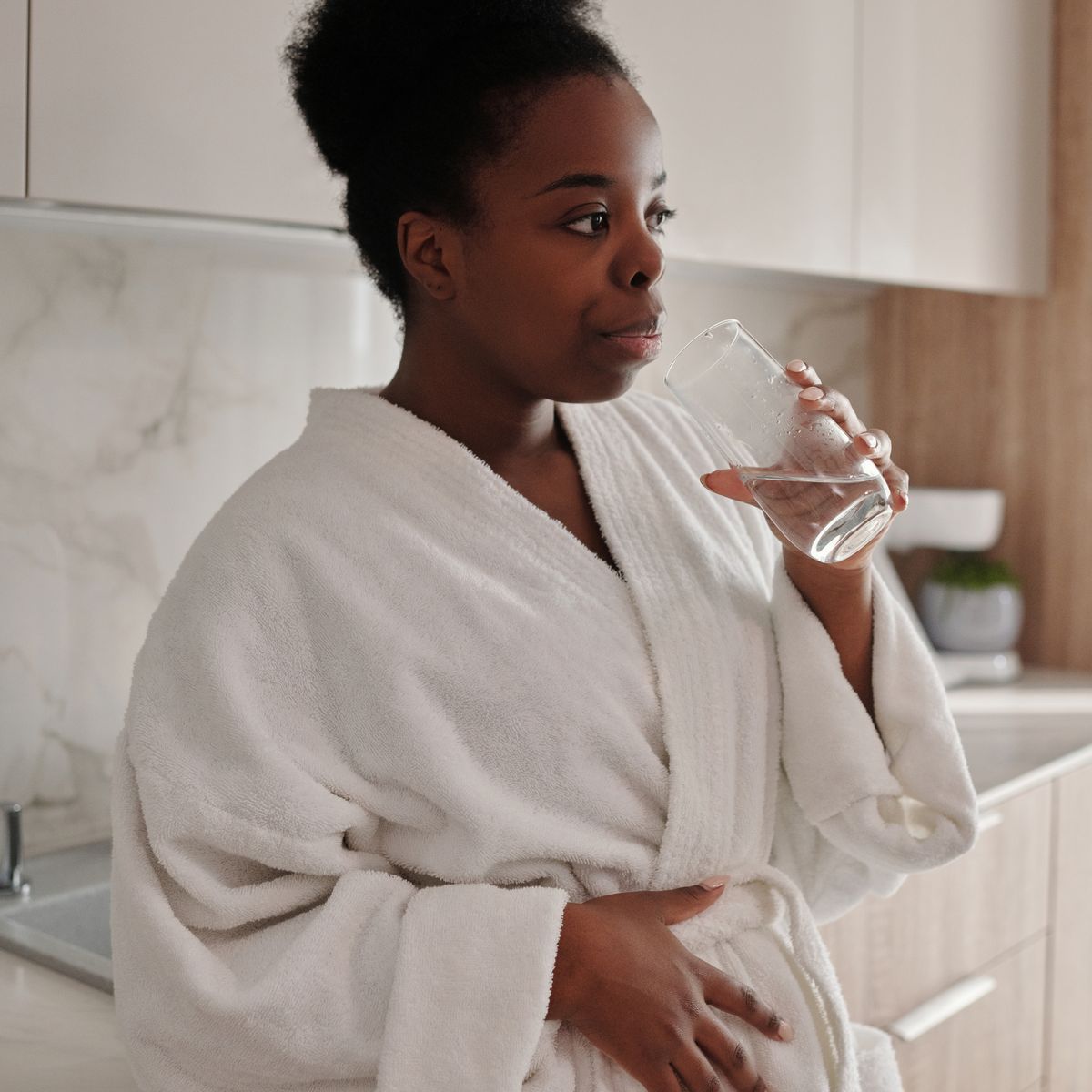 A woman drinking a glass of water in a bright kitchen