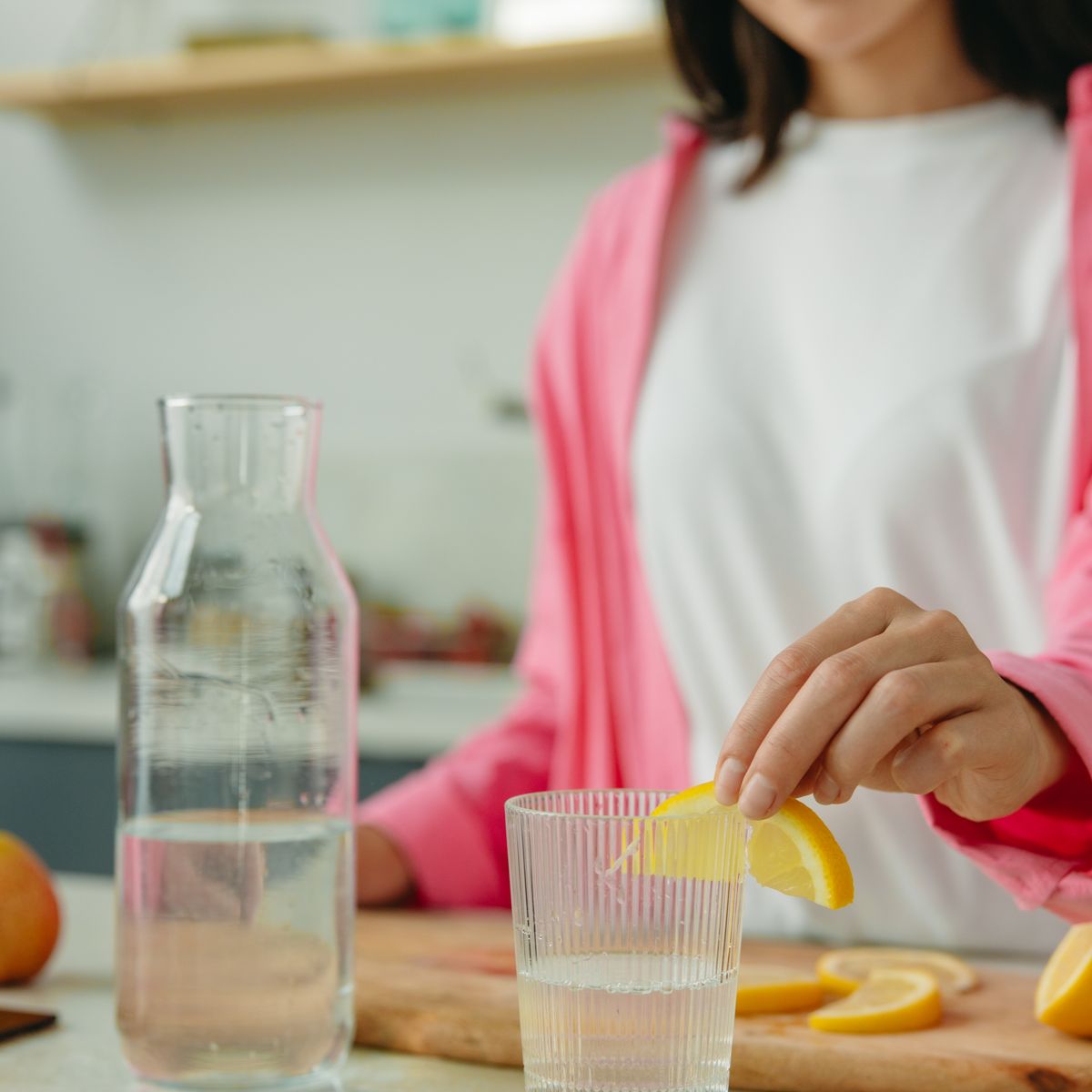Citrus slices being added to a glass carafe of water
