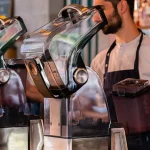 Barista using the Kuvings CB1000 vacuum blender behind a cafe counter