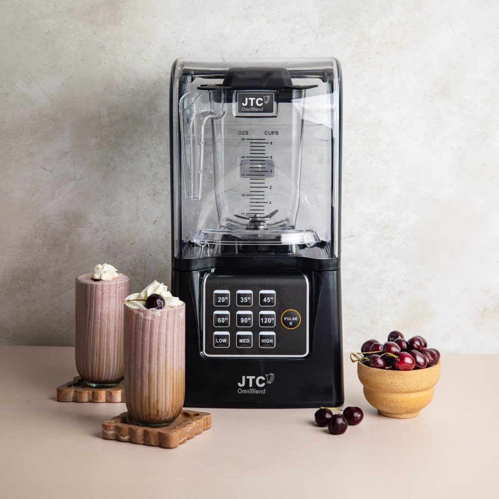 OmniBlend V+ commercial blender with sound cover beside two cherry smoothies