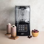 OmniBlend V+ commercial blender with sound cover beside two cherry smoothies