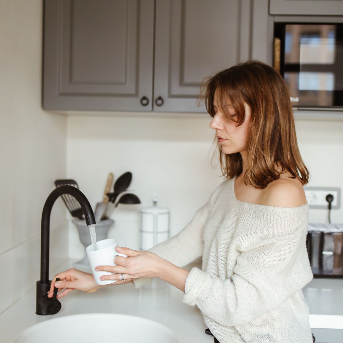 Woman filling a mug from a black kitchen faucet