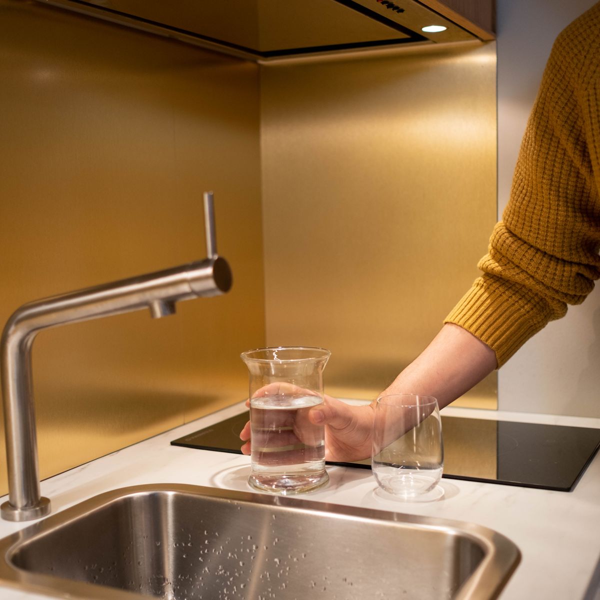 Person filling a glass of water at a kitchen sink