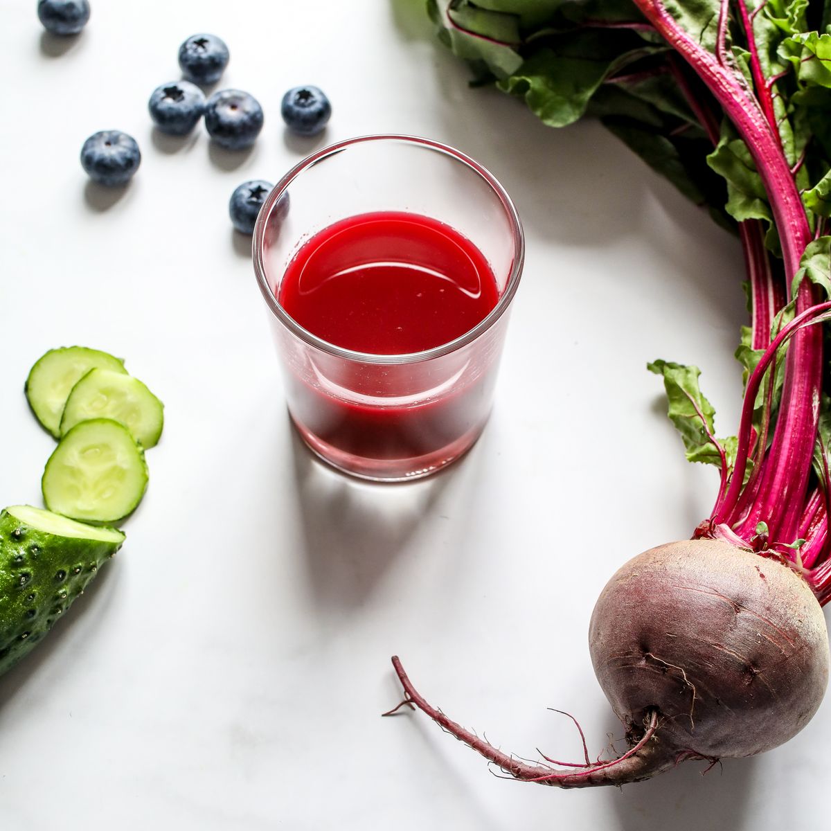 A glass of deep red beetroot juice beside a whole beetroot and cucumber