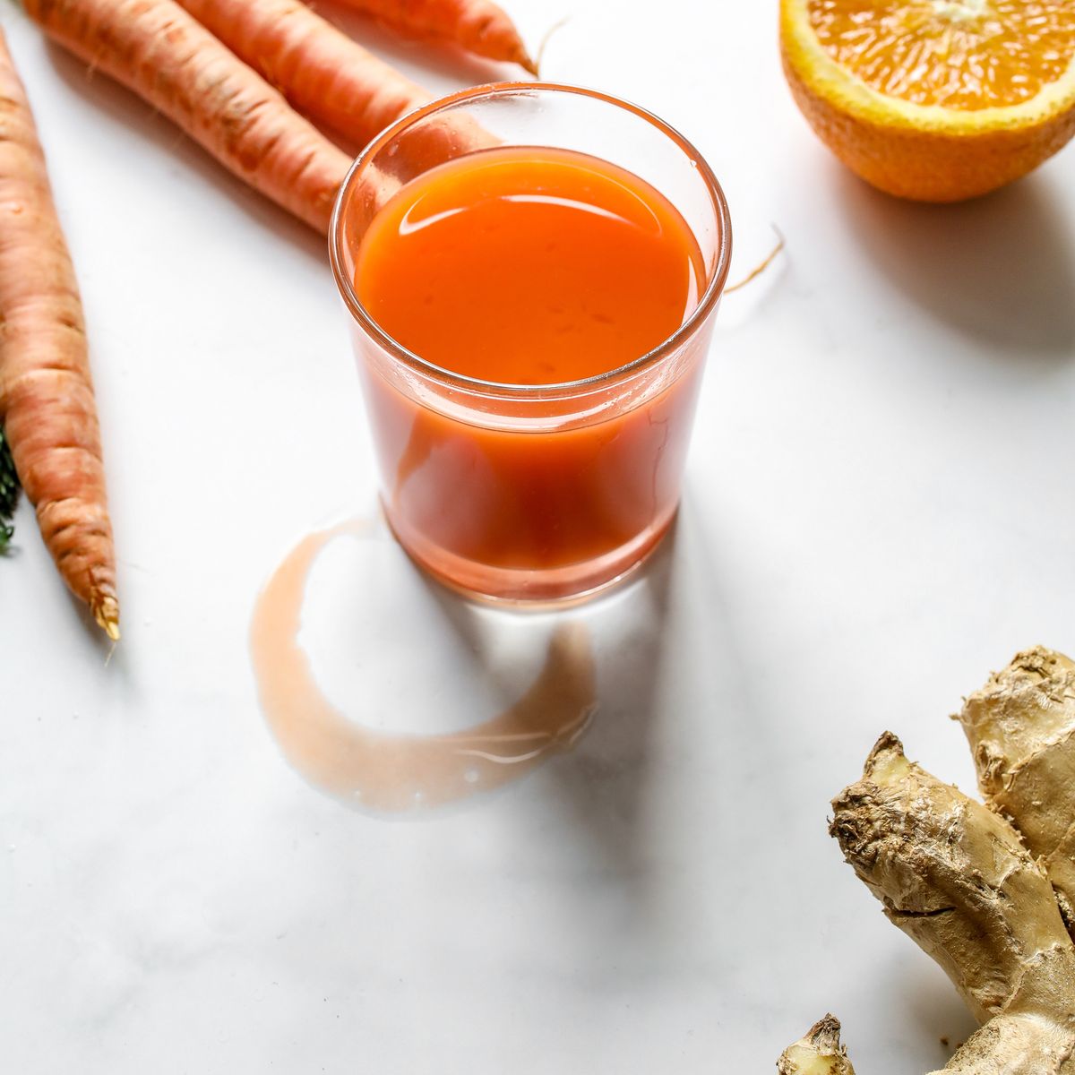 A glass of fresh carrot and orange juice beside whole carrots and ginger