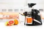 Sana 727 Supreme in Matte Black juicing carrot, with grapefruit and oranges on the counter