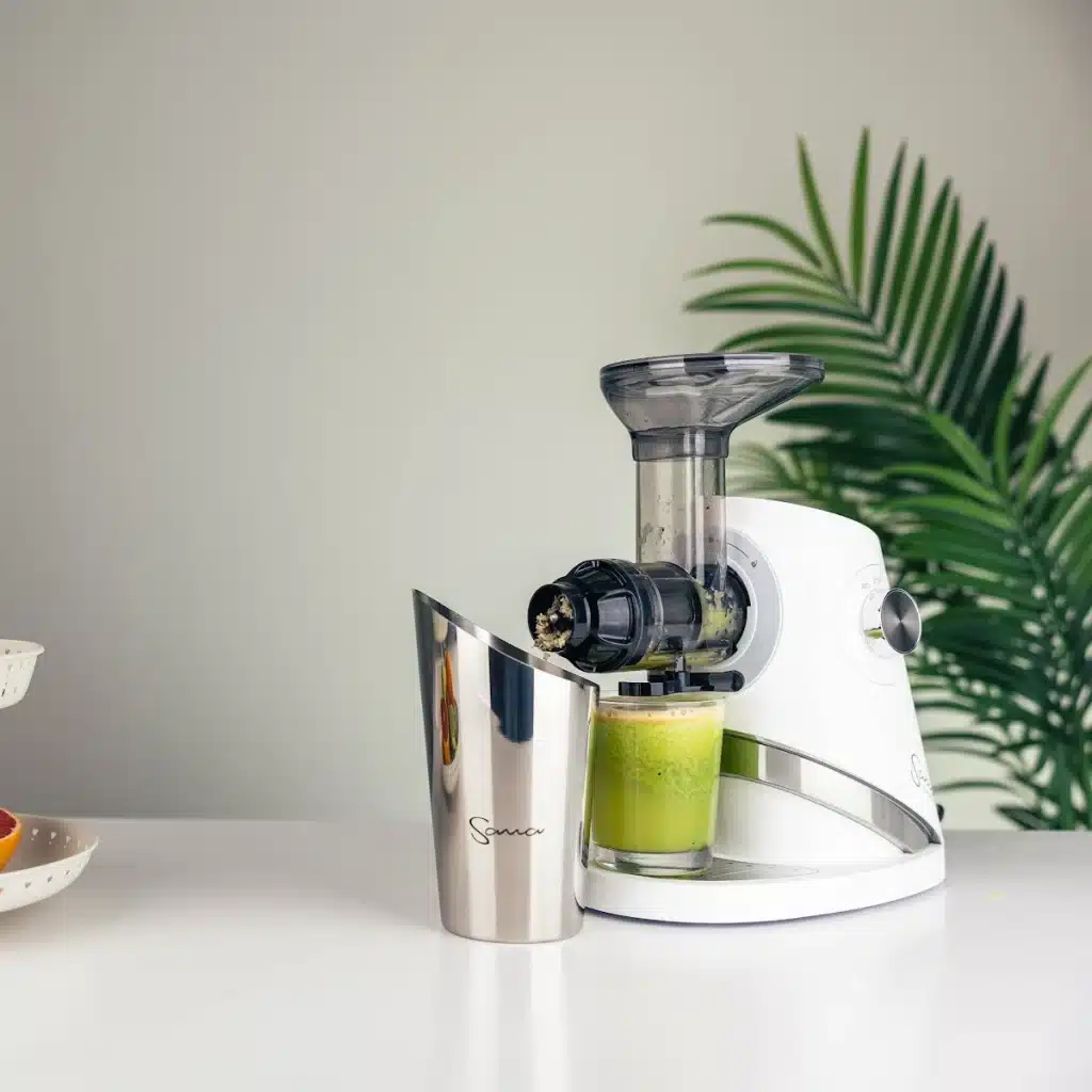 Sana 727 Supreme cold press juicer in Soft White with a glass of green juice